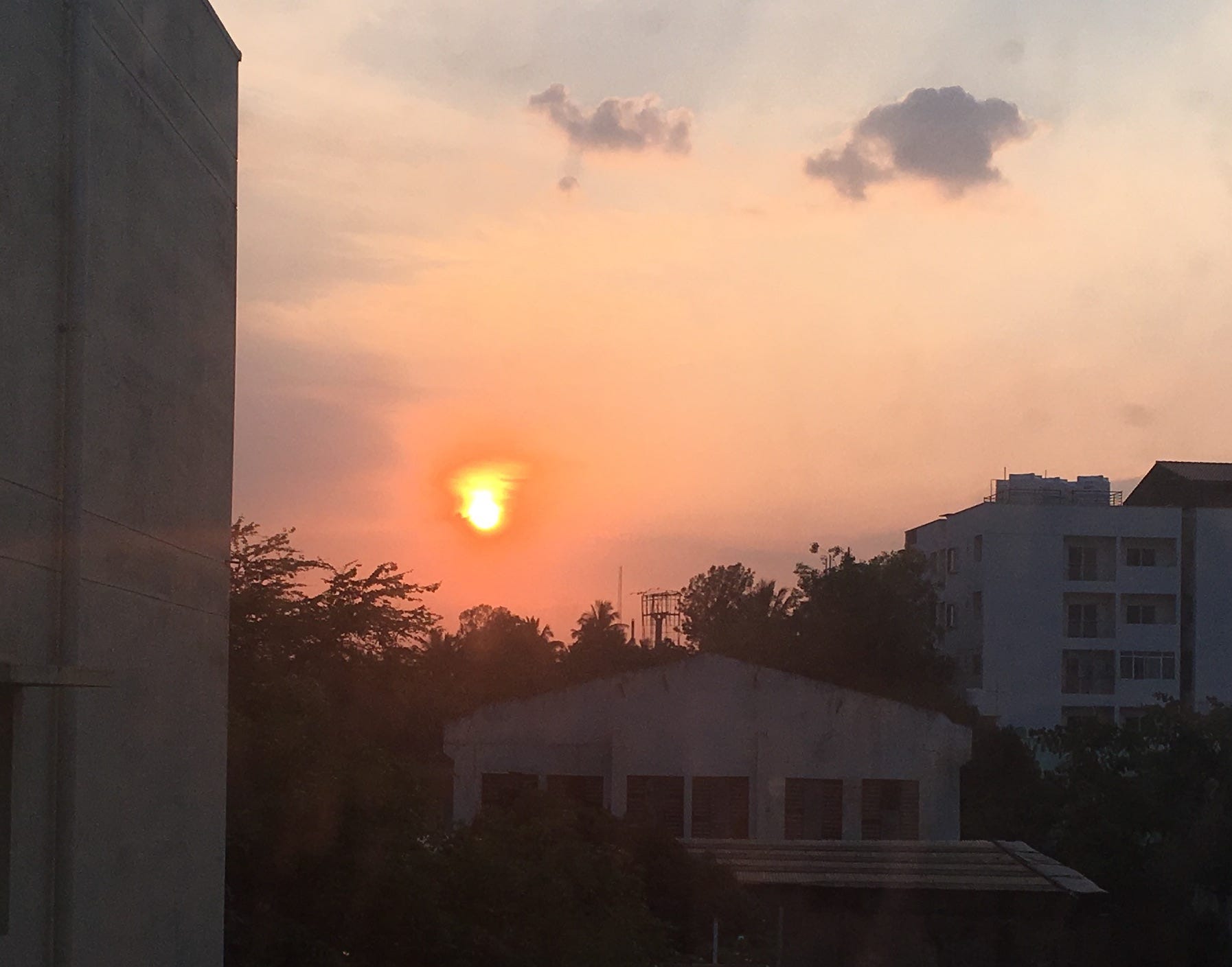 An atmosphere-induced smudgy looking Sun, which is about to set, as viewed from a residential area.