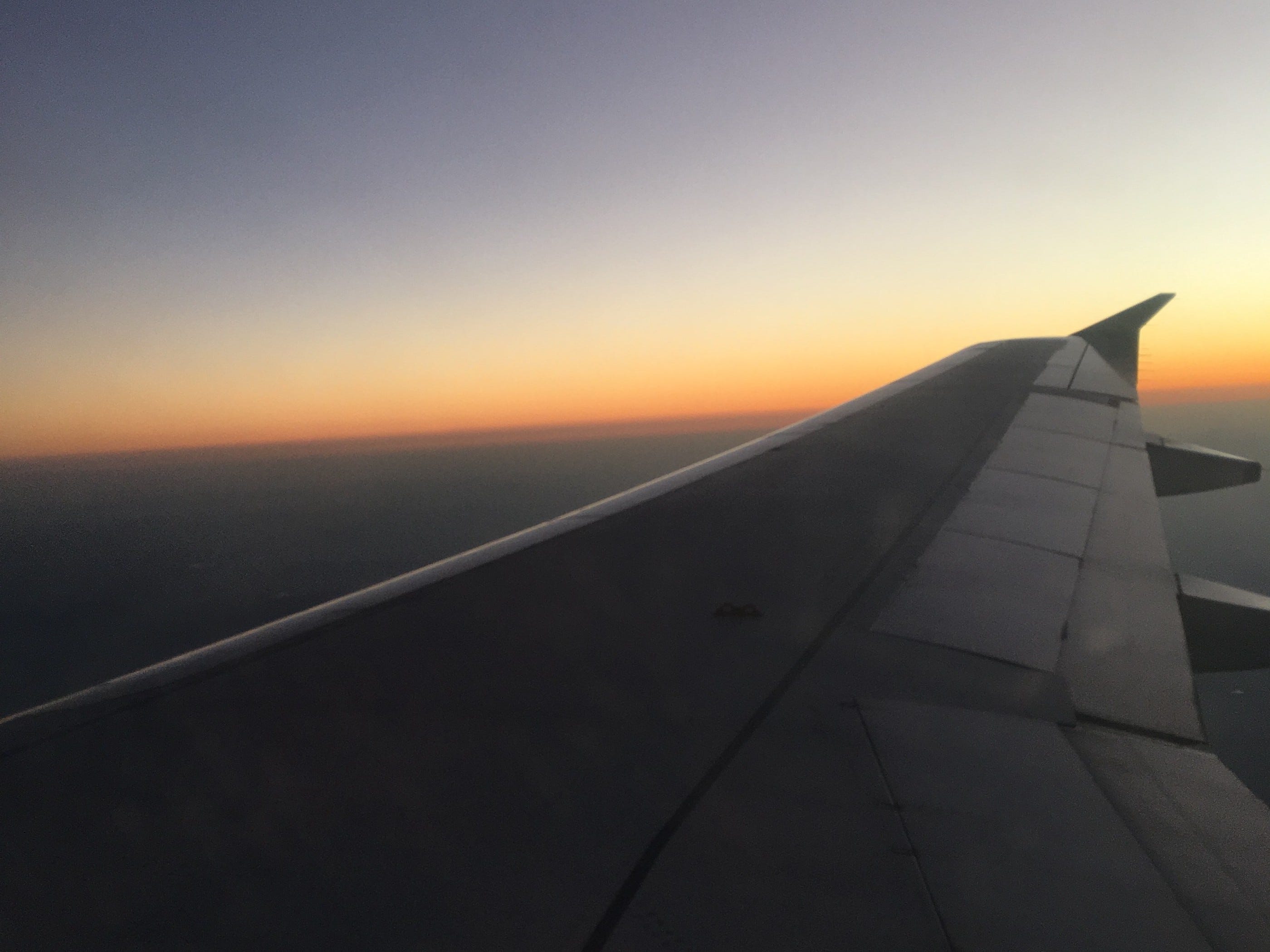 View of a delineated red dawn and blue sky from a plane, with a dark gray wing view.